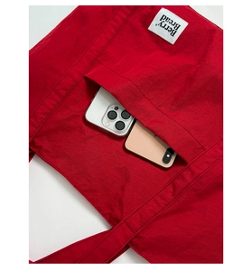 Detail shot of a red canvas tote bag showing the front pocket with two mobile phones inside