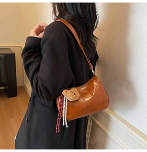 Detail of brown PU leather shoulder bag with plush bear charm and embossed logo text