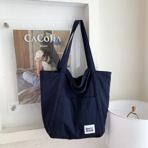 Detail view of navy blue canvas tote bag with side pocket and brand label on white wall