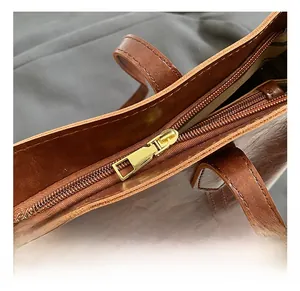 Close-up of golden zipper detail and handle stitching on vintage brown tote bag