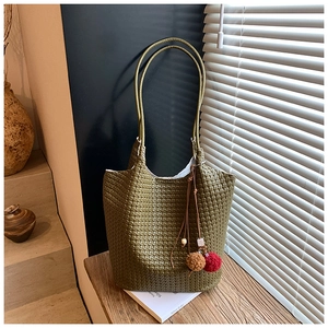 Detailed view of woven olive green leather tote bag with colorful pompom charm on a desk