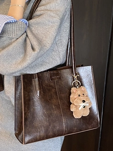 Vintage brown leather tote bag with plush charm, perfect for stylish everyday commuting