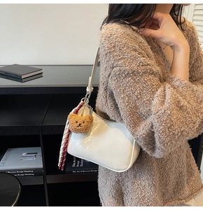 Detail of white glossy leather underarm bag with cute bear charm and striped scarf accent