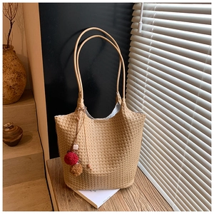 Close-up of woven bucket bag featuring pompom charms and slim round shoulder straps