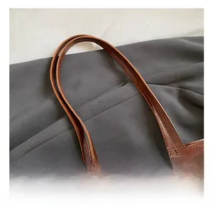 Detail view of brown tote bag handles with reinforcement stitching and bear charm