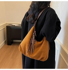 Close-up of brown suede hobo bag with long fringe tassels and floral charms on a model