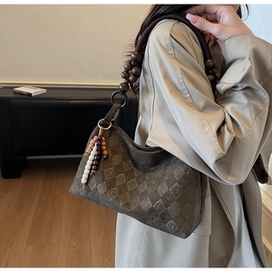 Detail of a brown suede shoulder bag with checkerboard embossing and wooden bead strap