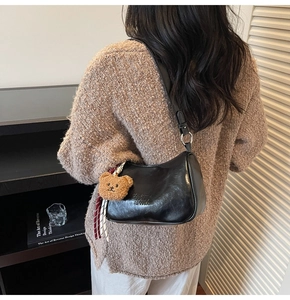 Close-up of black glossy leather shoulder bag with bear pendant and striped ribbon detail