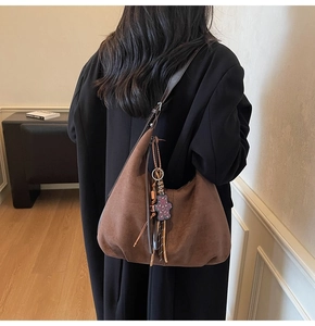 Detail of a large brown suede tote bag with fringe and purple bear charm on a model