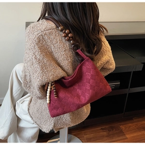 Detail of burgundy suede shoulder bag with wood bead strap and embossed texture
