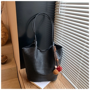 Detail of black woven tote bag with colorful pompom charm under window shutter shadows