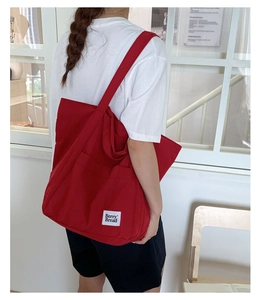 Detailed view of durable red canvas tote bag with white logo patch and wide strap