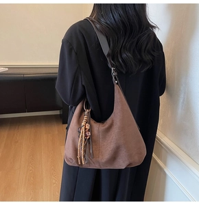 Close-up of brown suede hobo bag with woven tassels and wooden bead detail on shoulder
