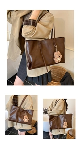 Detail view of a large dark brown faux leather tote bag with a plush bear charm and strap