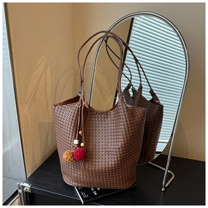 Detail shot of brown woven leather tote bag with decorative plush charms on a desk