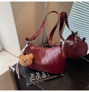 Detail of burgundy glossy leather underarm bag with teddy charm and elegant texture