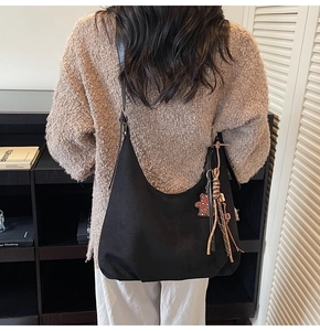 Close-up of black suede hobo bag with red leopard bear charm and braided tassel detail