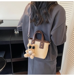 Detail van beige crossbody emmertas met bruine riemen en een pluchen beer hanger