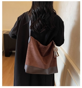 Rear view of brown suede bucket bag with leather trim and plush doll charm on shoulder