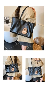 Detail of a large black leather tote bag with a cute brown bear plush charm and long straps