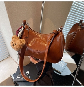 Detail of vintage brown shoulder bag with embossed logo and decorative plush bear charm