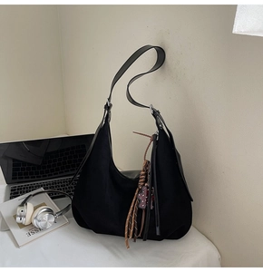 Macro shot of large black hobo shoulder bag with silver buckle and tassel detail
