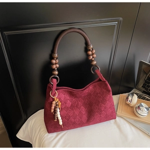 Detail view of burgundy faux suede shoulder bag with diamond stitching and bead handle