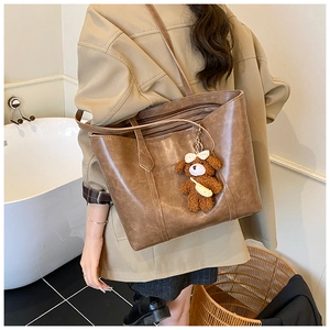 Detail of vintage brown tote bag featuring a cute plush bear charm with plaid bow