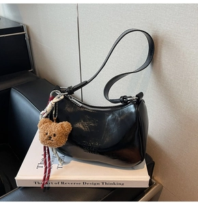 Detail of black glossy patent leather shoulder bag with bear charm and embossed logo lettering