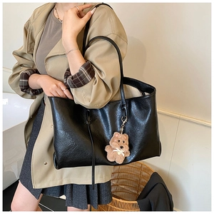 Close-up of black PU leather tote bag with a cute brown plush bear charm detail