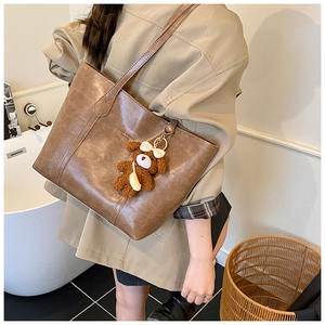 Detail of a large dark brown tote bag with a plush bear charm on a model's shoulder