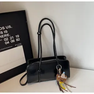 Détail du sac baguette en cuir noir brillant avec bandoulière nouée et breloque ourson