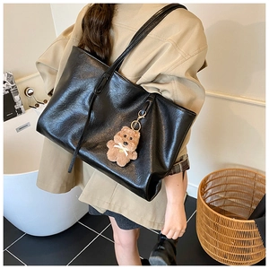 Detail view of large black tote bag with wax finish and cute plush bear charm