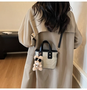 Detailweergave van beige emmertas met zwarte handvaten en pluche berenaccessoire