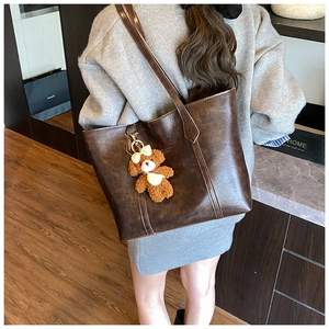 Detail of dark brown faux leather tote bag with vintage texture and cute bear pendant