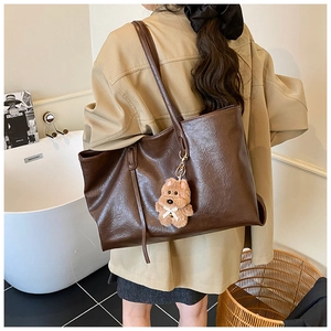 Close-up of a large dark brown tote bag with vintage texture and cute bear charm