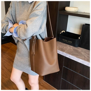 Model wearing dark brown lychee grain leather bucket bag with adjustable shoulder strap