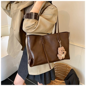 Detail of large dark brown tote bag with premium oil-wax leather texture and teddy bear charm