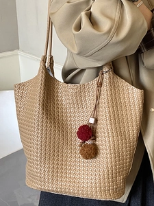 Brown woven tote bag with V-shaped texture and pom-pom charm on stylish khaki coat