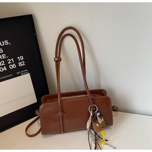 Détail d'un sac baguette en cuir marron foncé avec un ours et un pompon jaune