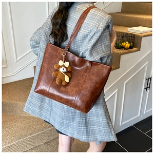 Close-up of brown faux leather tote bag with plush bear charm and embossed logo detail