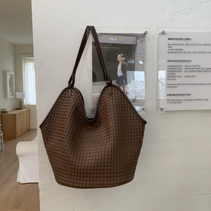 Detail shot of the deep brown leather woven bucket bag texture hanging on a white wall