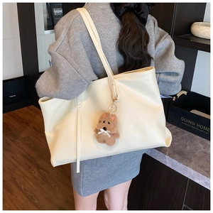 Detail view of a large cream tote bag with a cute brown plush dog charm for daily commute
