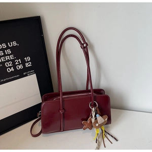 Détail du sac baguette en cuir verni bordeaux avec breloques étoile et ours sur table