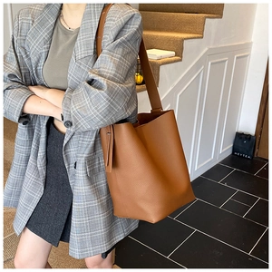 Brown faux leather bucket bag with pebbled texture shown on a shoulder in a lifestyle setting