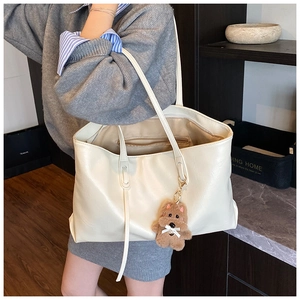 Detail of creamy beige tote bag on model showing large capacity and bear charm accessory