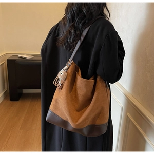 Caramel suede hobo bag shown in a lifestyle setting on a model's shoulder with pompom detail