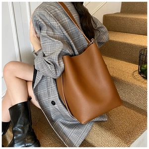 Close-up of a brown lychee pattern leather bucket bag worn by a model in a gray suit