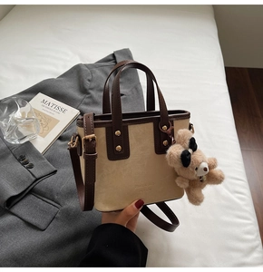 Detail van een beige emmertas met bruine rand en teddybeerbedeltje op wit beddengoed