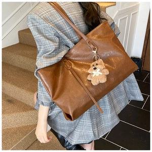 Detail of a large brown PU leather tote bag with a plush dog charm on a model